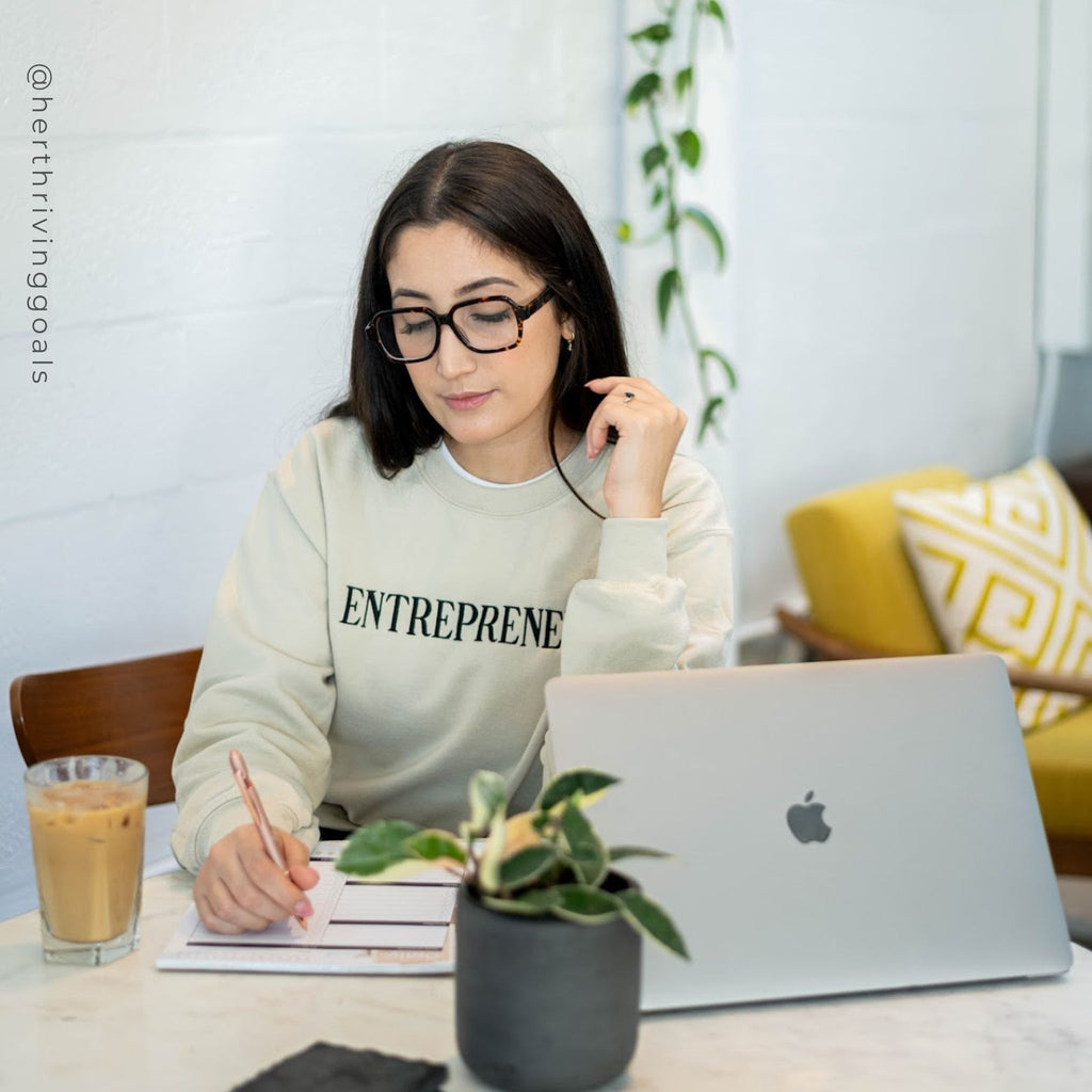 Entrepreneur Embroidered Crewneck Sand Sweatshirt On Woman. Woman writing on daily planner - Her Thriving Goals